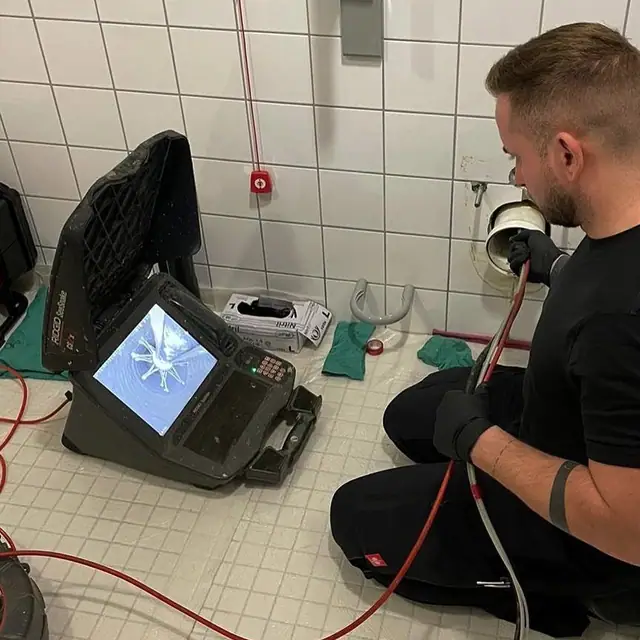 Monteur des Partnerbetriebs P&N schiebt die Kamera im gefliesten Sanitärraum in die Leitung